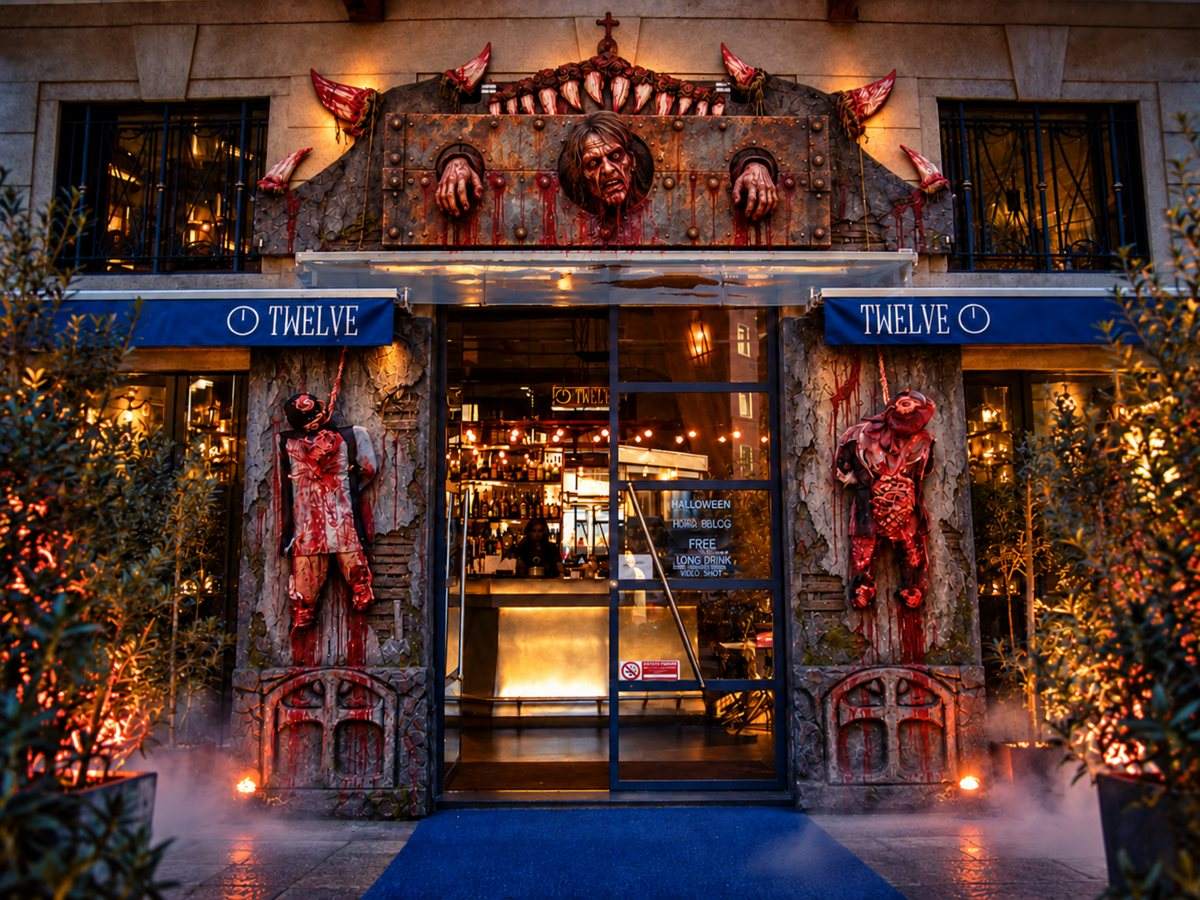 Ingresso di un locale allestito per Halloween con scenografie horror scolpite e dipinte, nebbia e luci calde